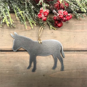 Könnte beinhalten: Ein silberner Esel-Anhänger aus Metall mit rustikalem Finish. Der Anhänger hat einen Bindfaden zum Aufhängen und ist perfekt für einen Weihnachtsbaum oder eine Bauernhausdekoration.