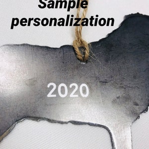K&ouml;nnte beinhalten: Ein silberner Metallschild in Form eines Hundes mit dem Jahr 2020 eingraviert. Das Schild h&auml;ngt an einer Schnur aus Jute.
