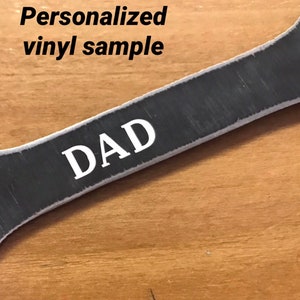 K&ouml;nnte beinhalten: Ein personalisierter Schraubenschl&uuml;ssel aus Metall mit dem Wort "DAD" in wei&szlig;er Vinylfolie.