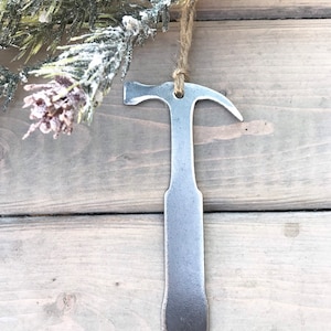 Könnte beinhalten: Ein silberner Hammer-Anhänger aus Metall mit rustikalem Finish. Der Anhänger hängt an einer Schnur aus Jute.