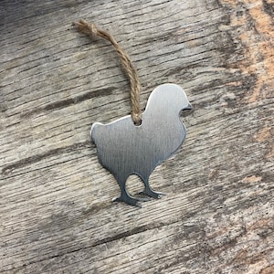 May include: A silver metal chick ornament with a brown twine hanger. The chick is a simple silhouette with a rounded body and small feet.