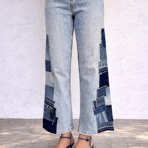 Op de afbeelding: Lichtblauwe spijkerbroek met een hoge taille en wijde pijpen. De buitenste zijnaden zijn versierd met een verticaal patchwork-ontwerp bestaande uit verschillende tinten blauwe denim stofresten met gerafelde randen.
