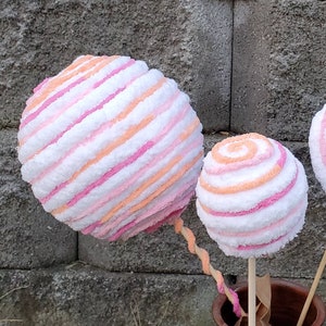 May include: Two large pink and orange striped yarn balls on wooden sticks. The balls are fluffy and look like cotton candy.