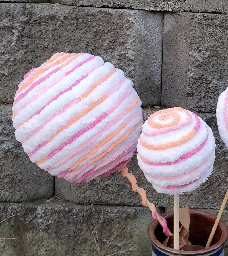 May include: Two large pink and orange striped yarn balls on wooden sticks. The balls are fluffy and look like cotton candy.