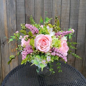 May include: A pink and green floral arrangement in a clear glass vase. The arrangement features pink roses, green hydrangeas, and pink and green foliage.