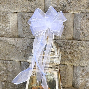 May include: A white tulle bow with a large, full, and fluffy shape. The bow is tied around a decorative, ornate, silver-colored lantern.