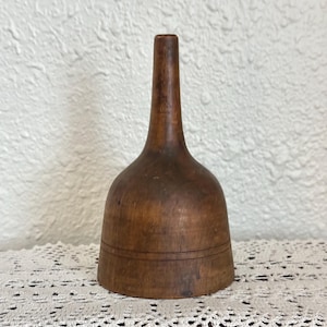 May include: A vintage, handcrafted wooden funnel with a flared base and a long, slender neck. The funnel is made of a warm, medium-toned wood and features a decorative groove around the base. This kitchenware item is ideal for pouring liquids or dry ingredients.