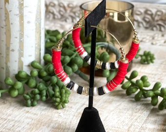 May include: Red, white, and black beaded hoop earrings with gold accents. The earrings are displayed on a black stand.