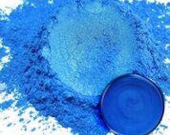 Op de afbeelding: Een close-up van een helderblauw pigmentpoeder. Het poeder is uitgespreid op een wit oppervlak, met een klein monster van het poeder in een ronde container.