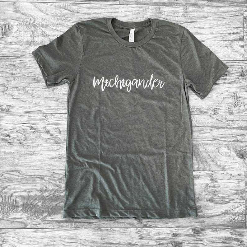 Puede incluir: Una camiseta gris jaspeada con la palabra "Michigander" en escritura blanca en el pecho. La camiseta tiene cuello redondo y mangas cortas. La tela parece suave y c&oacute;moda.