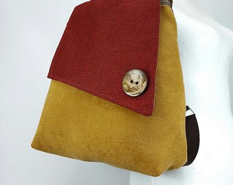 May include: A mustard yellow and red canvas backpack with a large wooden button. The backpack has a flap closure and a brown strap.