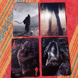 Puede incluir: Cuatro cartas de juego con un tema oscuro y g&oacute;tico. Las cartas son el 10 de diamantes, el jinete de tr&eacute;boles, el jinete de picas y el jinete de corazones. El 10 de diamantes presenta una figura encapuchada con una guada&ntilde;a en un entorno lluvioso. El jinete de tr&eacute;boles presenta una figura sombr&iacute;a con un arma en un entorno oscuro y brumoso. El jinete de picas presenta una criatura con un ojo grande y dientes afilados. El jinete de corazones presenta una criatura con una cabeza grande y una postura encorvada.