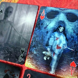 Puede incluir: Dos cartas de juego, un 9 de tr&eacute;boles y un as de corazones, con ilustraciones de tem&aacute;tica de pel&iacute;culas de terror. El 9 de tr&eacute;boles presenta una imagen borrosa de una figura en un bosque. El as de corazones presenta una figura con una m&aacute;scara de hockey y sosteniendo un cuchillo ensangrentado.