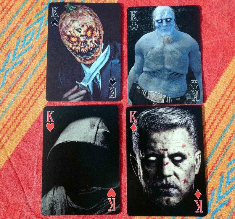 Puede incluir: Cuatro cartas de juego con diferentes reyes. La primera carta muestra un rey con una cabeza de calabaza sosteniendo un cuchillo. La segunda carta muestra un rey con un cuerpo azul y una corona. La tercera carta muestra un rey con una figura negra encapuchada. La cuarta carta muestra un rey con una cara que tiene una expresi&oacute;n seria.