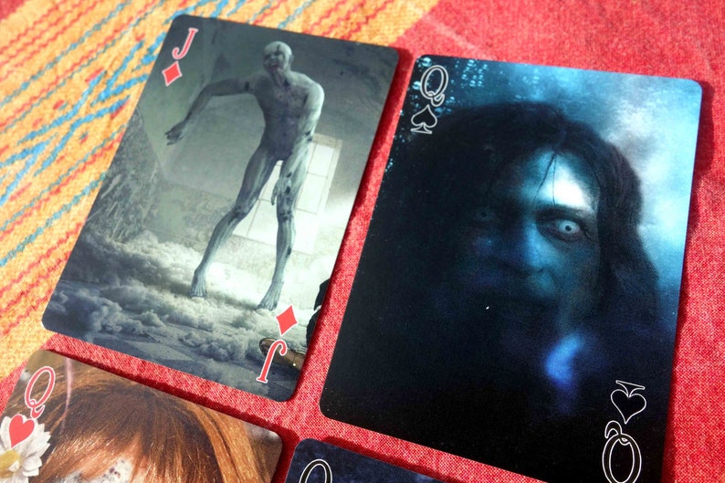 Puede incluir: Cuatro cartas de juego de una baraja de tem&aacute;tica de terror. Las cartas son el Jack de Diamantes, la Reina de Espadas, la Reina de Corazones y la Reina de Tr&eacute;boles. Cada carta presenta una imagen aterradora diferente.