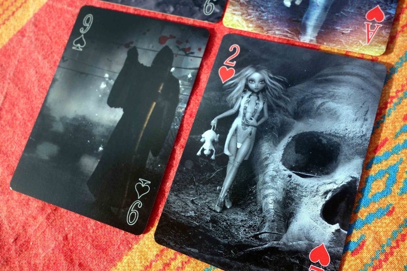 Puede incluir: Dos cartas de juego, un 9 de picas y un 2 de corazones, con im&aacute;genes oscuras y g&oacute;ticas. El 9 de picas presenta una figura sombr&iacute;a con una guada&ntilde;a, mientras que el 2 de corazones representa a una mujer con una calavera y un animal peque&ntilde;o.