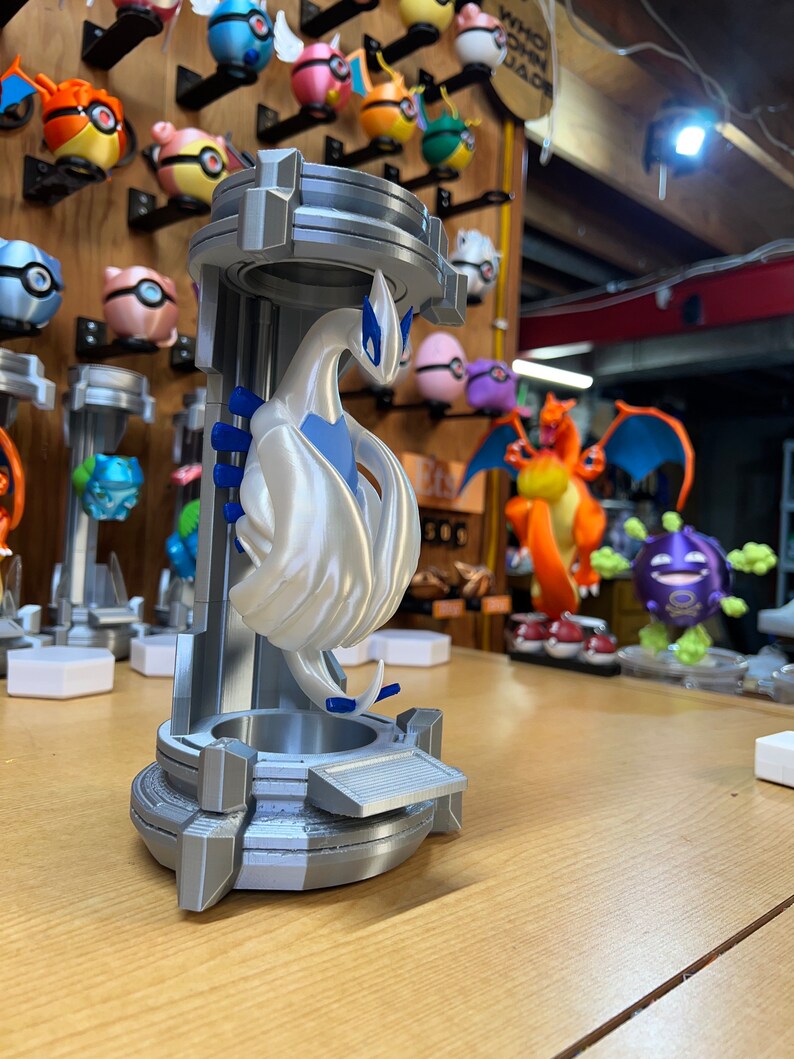 Puede incluir: Una figura de Pok&eacute;mon impresa en 3D de color blanco de un Pok&eacute;mon p&aacute;jaro legendario, con detalles azules, de pie sobre un pedestal plateado. La figura est&aacute; en una pose con las alas extendidas.