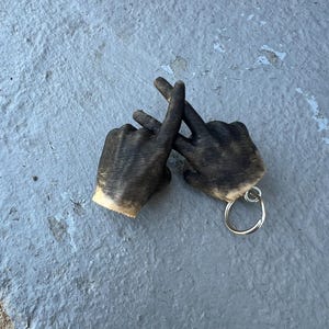 May include: A wooden keychain shaped like two hands making the 'W' hand gesture. The keychain is painted black and has a silver key ring.