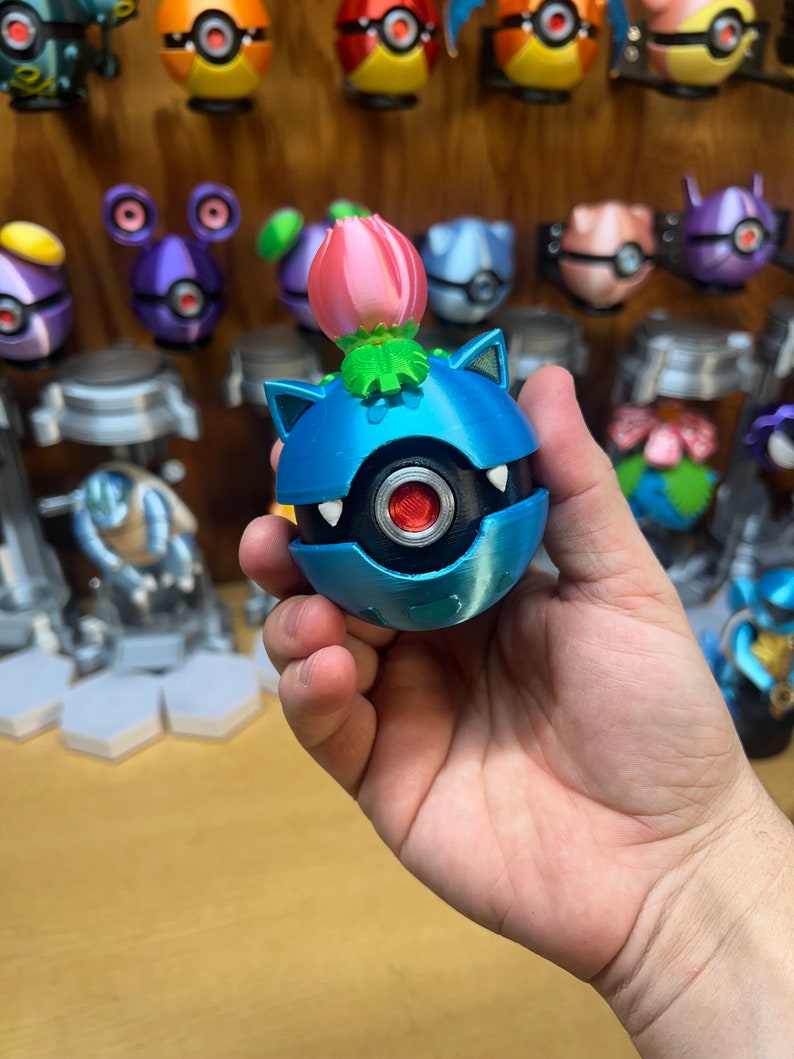 Puede incluir: Una figura Pok&eacute;mon impresa en 3D de color azul y plateado con una flor rosa en la parte superior. La figura est&aacute; siendo sostenida en la mano de una persona.