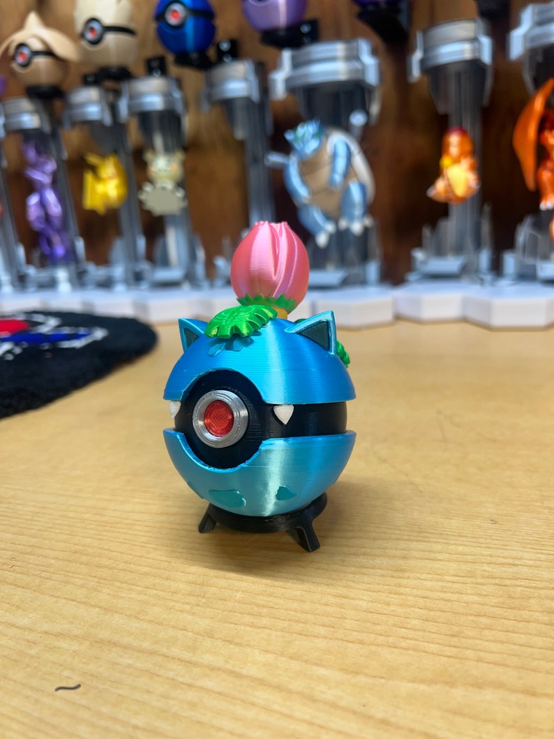 Puede incluir: Una figura de Pokemon Snorlax impresa en 3D de color azul y negro con una flor rosa en la parte superior. La figura est&aacute; de pie sobre una peque&ntilde;a base negra.