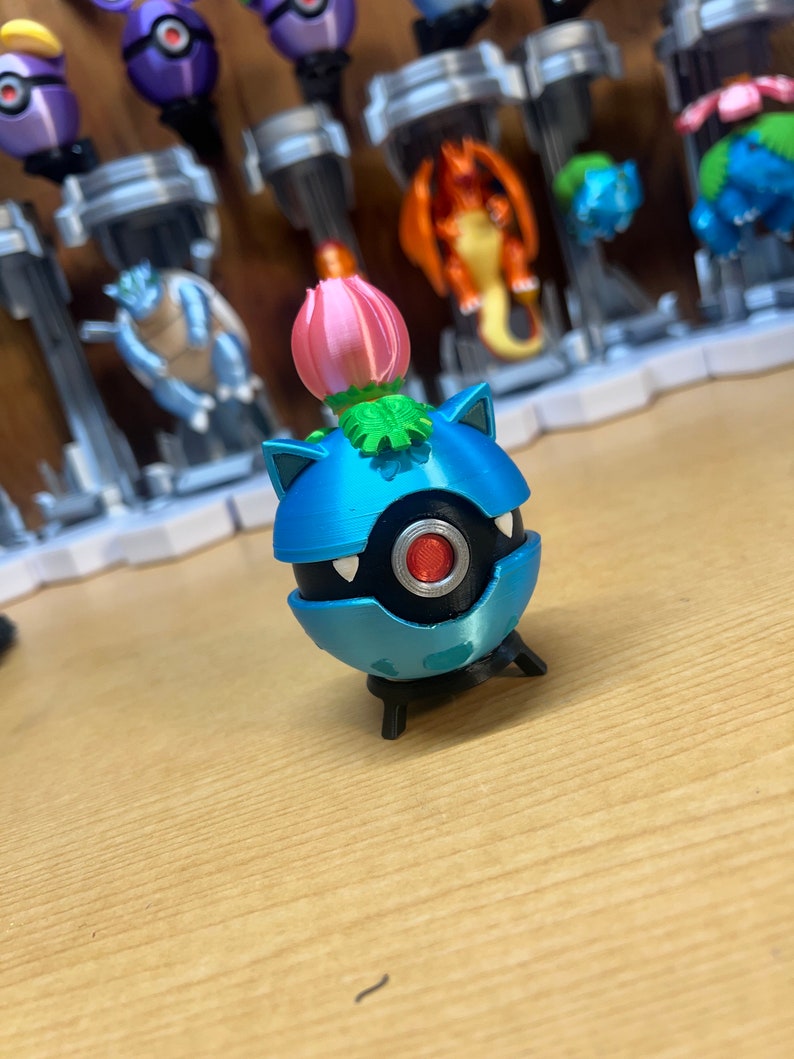 Puede incluir: Una figura de Pok&eacute;mon azul y negro con una flor rosa en la parte superior. La figura est&aacute; de pie sobre una superficie de madera.