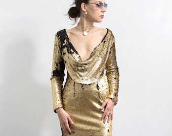 May include: A gold sequin mini dress with long sleeves and a cowl neckline. The dress has black accents on the neckline and sleeves. The person is wearing black heels.