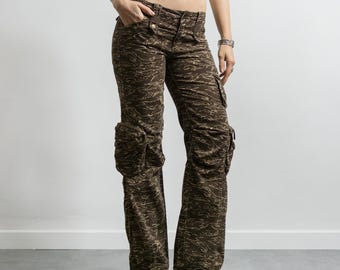 May include: Brown cargo pants featuring a dark tiger stripe camouflage pattern, multiple side pockets, a button and zipper fly closure, and adjustable drawstring ties at the bottom hems of the pant legs for a customizable fit.