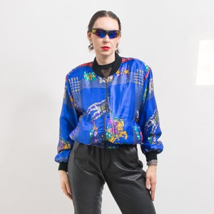 May include: A blue satin bomber jacket with a colorful print of horses and riders. The jacket has a zipper closure and a stand-up collar.