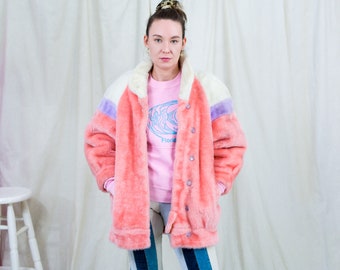 May include: A pink faux fur jacket with white and purple accents. The jacket has a button closure and is worn over a pink long-sleeved shirt with a blue fish graphic and the word "Florida".