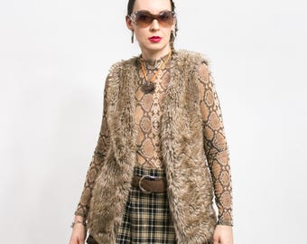 May include: A brown faux fur vest with a brown and black plaid skirt. The vest has a zipper closure and a stand-up collar. The person is wearing a brown snake print mesh top and clear framed sunglasses.