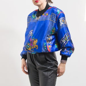 May include: A blue satin bomber jacket with a colorful equestrian print. The jacket has a zipper closure and a stand-up collar.