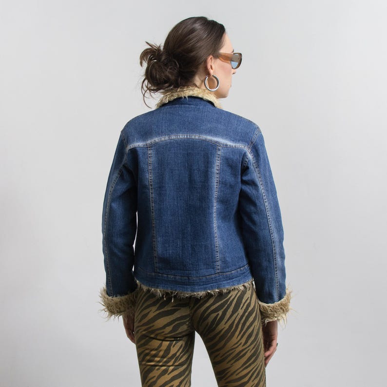 Peut inclure: Veste en jean bleue avec col et poignets en fausse fourrure beige. La veste a un design classique avec une fermeture boutonn&eacute;e et un d&eacute;lavage clair. La personne porte un pantalon &agrave; imprim&eacute; z&eacute;br&eacute;.