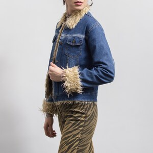 Peut inclure: Veste en jean bleue avec garniture en fausse fourrure beige sur le col, les poignets et l'int&eacute;rieur. La veste a deux poches poitrine et une fermeture boutonn&eacute;e. Le mod&egrave;le porte un bracelet et un pantalon &agrave; imprim&eacute; z&eacute;br&eacute;.