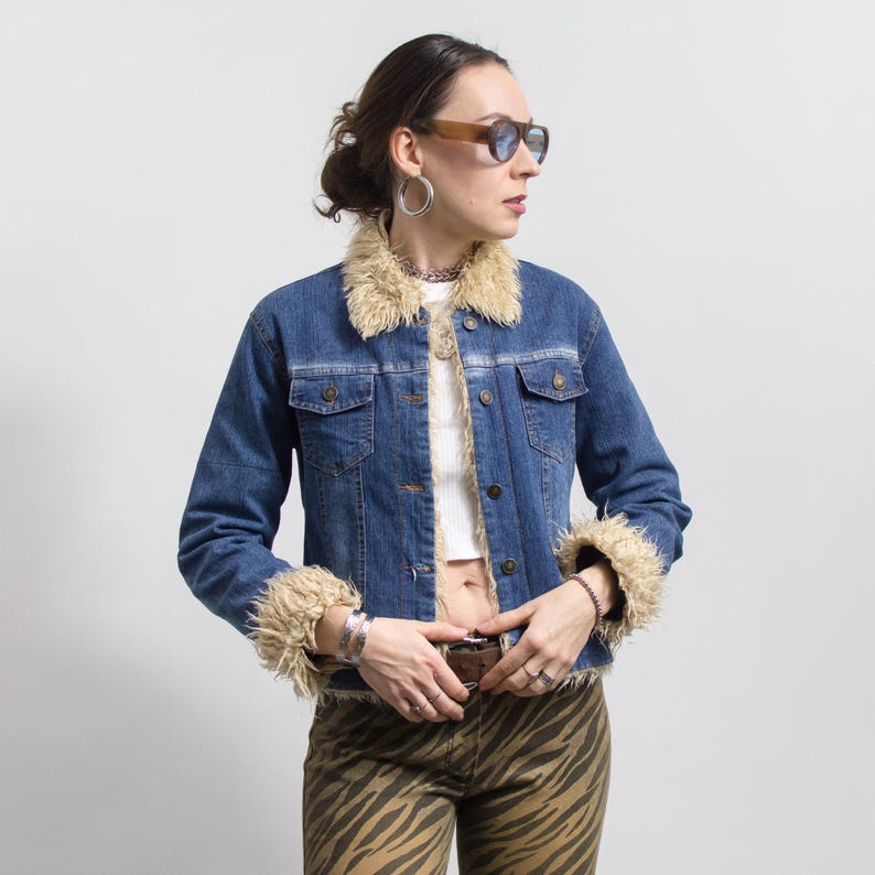 Peut inclure: Veste en jean bleue avec col et poignets en fausse fourrure beige. La veste a deux poches poitrine et une fermeture boutonn&eacute;e. La personne porte des lunettes de soleil et un haut blanc. Le pantalon est imprim&eacute; z&egrave;bre.