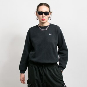 May include: A black sweatshirt with a white Nike swoosh logo. The sweatshirt is paired with black pants. The person is wearing sunglasses and a silver necklace.