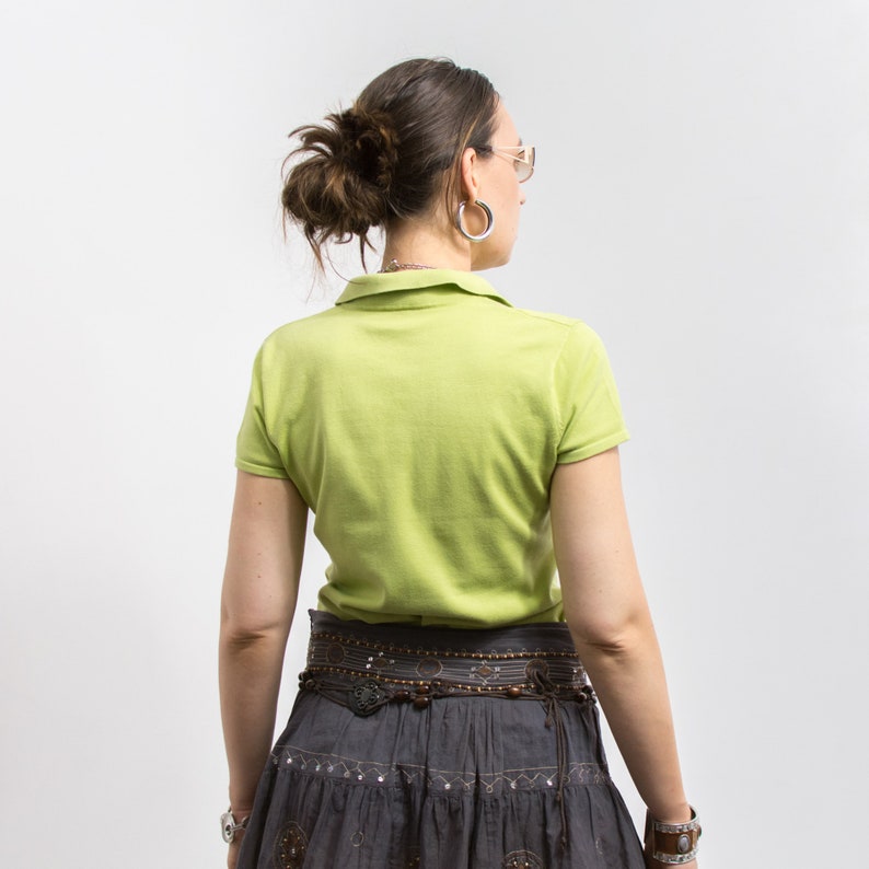 K&ouml;nnte beinhalten: Ein limegr&uuml;nes, kurz&auml;rmeliges Poloshirt mit einem braunen Perleng&uuml;rtel und einem grauen Rock mit Blumenmuster.