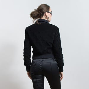 Puede incluir: Chaqueta bomber negra de pana con dobladillo y pu&ntilde;os acanalados. La chaqueta tiene un cuello alto y se combina con pantalones negros. El conjunto es un conjunto monocrom&aacute;tico elegante, adecuado para un look casual o semiformal.