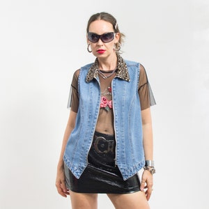 May include: A woman wearing a light blue denim vest with a leopard print collar, a black mesh top with a floral design, a black leather skirt, and black sunglasses.