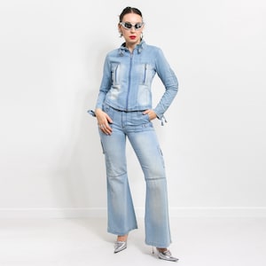 Könnte beinhalten: Eine hellblaue Jeansjacke und eine passende Hose mit mehreren Taschen und Reißverschlussdetails. Die Jacke hat einen hohen Kragen und einen Reißverschluss. Die Hose ist ausgestellte und hat eine lockere Passform.