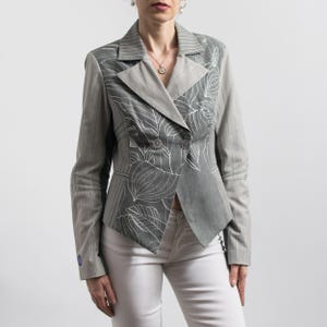 May include: A grey blazer with a pinstripe pattern on the sleeves and a solid grey front panel. The front panel features a white floral design. The blazer has a double-breasted closure and a notched lapel.