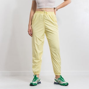 May include: Yellow nylon pants with a drawstring waist and elastic cuffs. The pants have a relaxed fit and are perfect for casual wear.