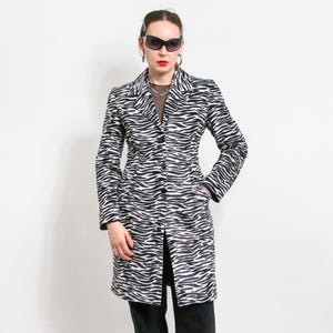 Op de afbeelding: Een zwart-witte jas met zebraprint, een reverskraag en een knoopsluiting. De jas met lange mouwen heeft een getailleerde pasvorm en zakken. De jas is knielang.