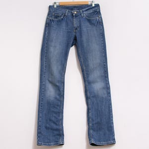 Peut inclure: Un jean en denim bleu suspendu &agrave; un cintre en bois. Le jean a une coupe droite classique &agrave; cinq poches, une fermeture &agrave; bouton et fermeture &eacute;clair. Le denim pr&eacute;sente un d&eacute;lavage d&eacute;color&eacute; avec des d&eacute;tails subtils.