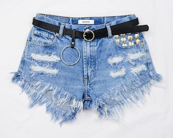May include: Light blue denim shorts with frayed edges and a black belt with silver studs. The shorts have several distressed areas and a silver ring attached to the belt.