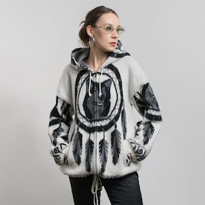May include: A white hooded zip-up sweater with a black and white dreamcatcher design on the front. The dreamcatcher features a wolf's face in the center and hanging feathers. The sleeves have black and white patterns and wolf images.