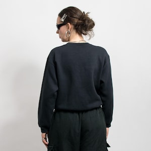 May include: A black crew neck sweatshirt and black cargo pants. The person is wearing sunglasses, silver hoop earrings, a silver chain necklace, and a silver hair clip. The person is facing away from the camera.