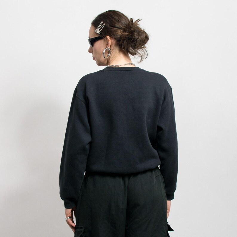 May include: A black crew neck sweatshirt and black cargo pants. The person is wearing sunglasses, silver hoop earrings, a silver chain necklace, and a silver hair clip. The person is facing away from the camera.