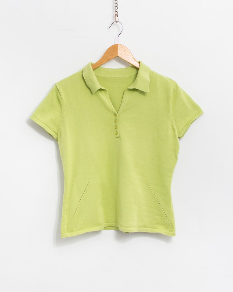 K&ouml;nnte beinhalten: Ein hellgr&uuml;nes, kurz&auml;rmeliges Poloshirt mit Knopfleiste und einem Holzb&uuml;gel.