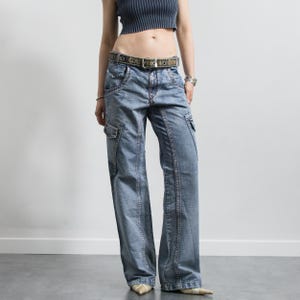 Op de afbeelding: Lichtblauwe denim cargobroek met meerdere zakken en een wijde pijp. De broek heeft een vervaagde wassing en wordt gedragen met een riem met patroon en een gestreepte crop top. De broek is een casual stijl.