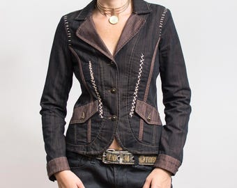 May include: Dark denim jacket with brown accents on the collar, pockets, and cuffs. The jacket features white stitching details and two front pockets. It has a button-up closure and a belt with text.